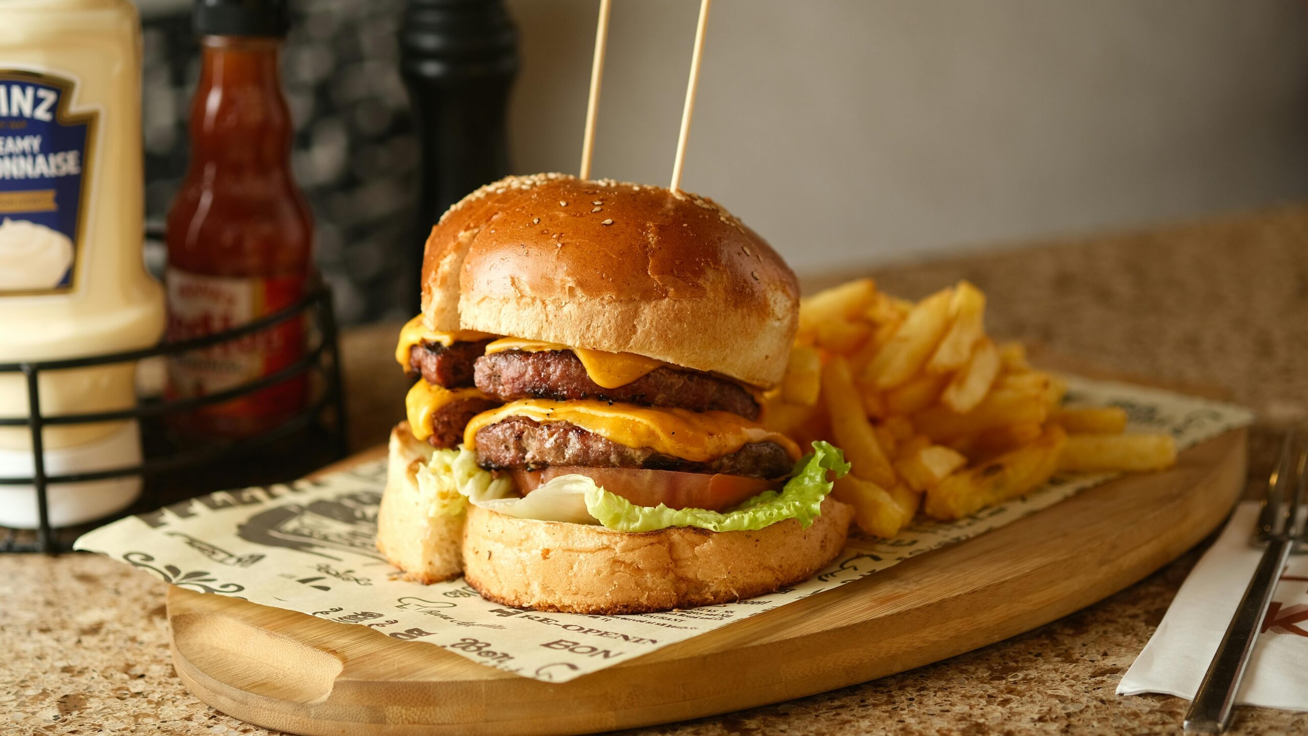 Saftiger Cheeseburger mit Doppel-Patties und Pommes frites serviert auf einem Holzbrett.