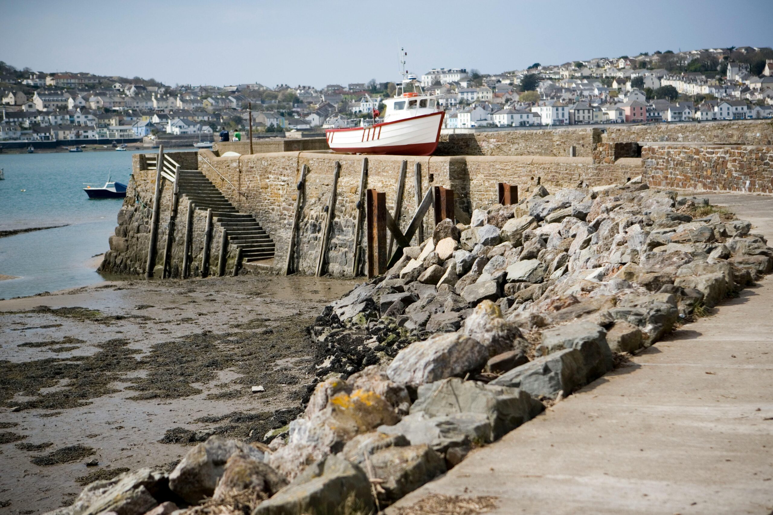 Eine friedliche Hafenszene in England mit einem am Steinpier angedockten Boot und einem Blick auf die Stadt in der Ferne.