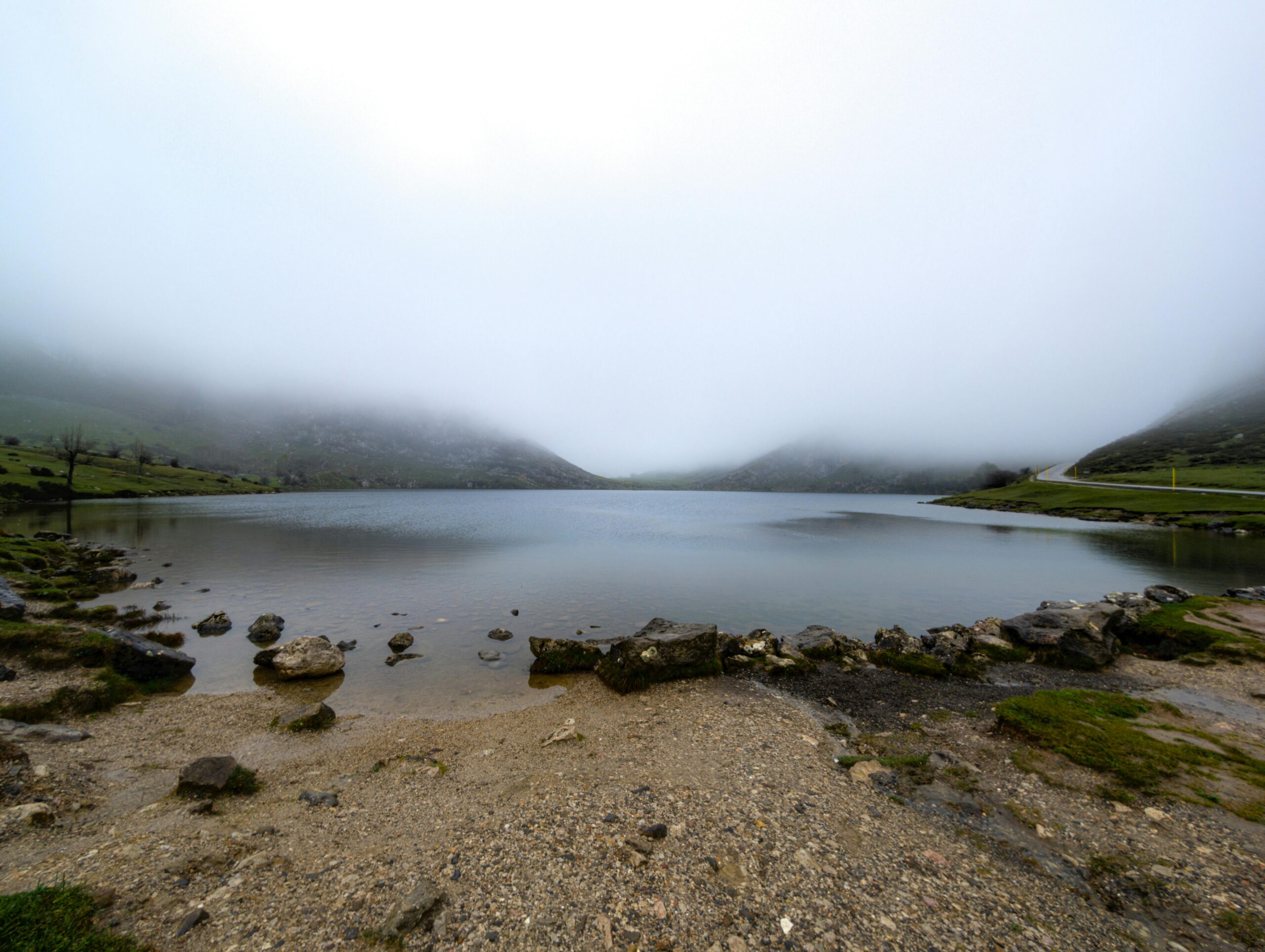 Heiterer, nebliger Morgen am Enolsee, Asturien, mit Nebel über der friedlichen Berglandschaft.