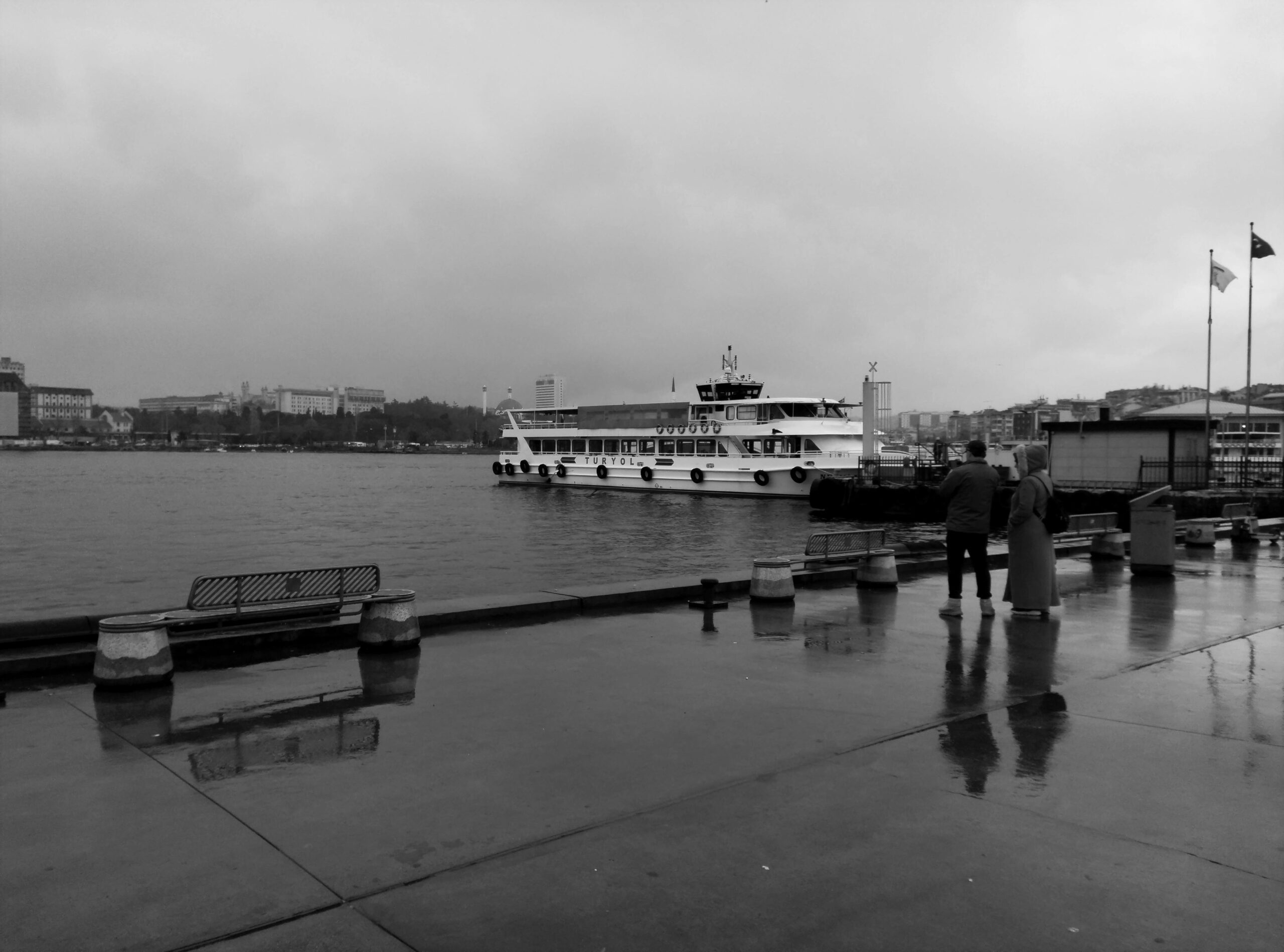 Schwarz-Weiß-Ansicht einer Fähre und Menschen an einem Dock in Istanbul an einem bewölkten Tag.