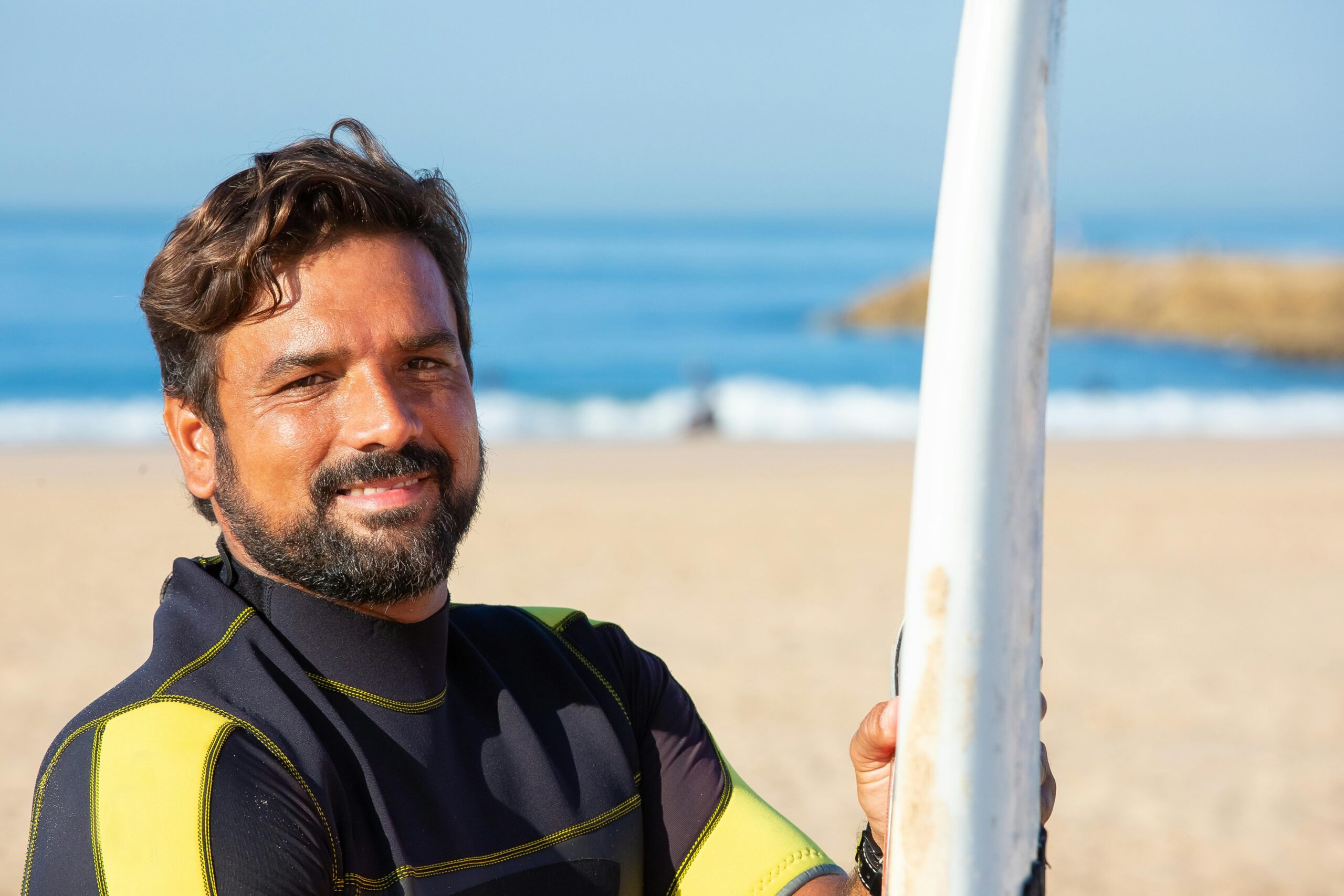 Glücklicher Ethnischer Männlicher Surfer Mit Surfbrett, Das Auf Sonniger Küste Steht