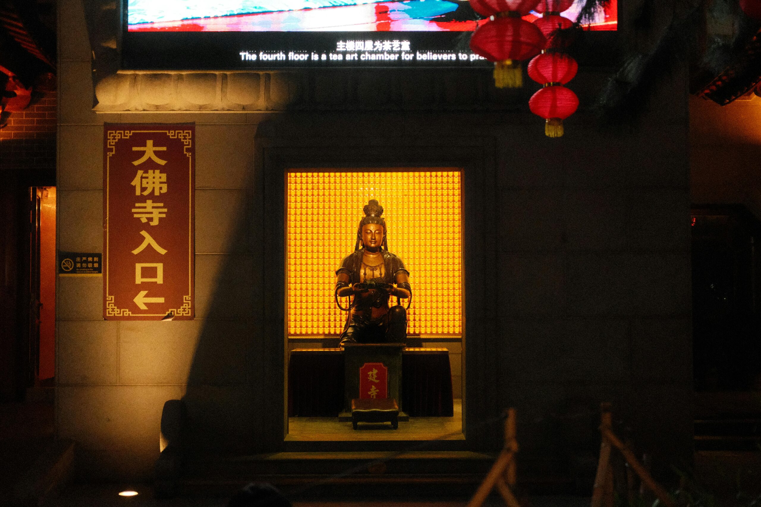 Eine beleuchtete Buddha-Statue am Eingang eines Tempels, nachts von Laternen umgeben.