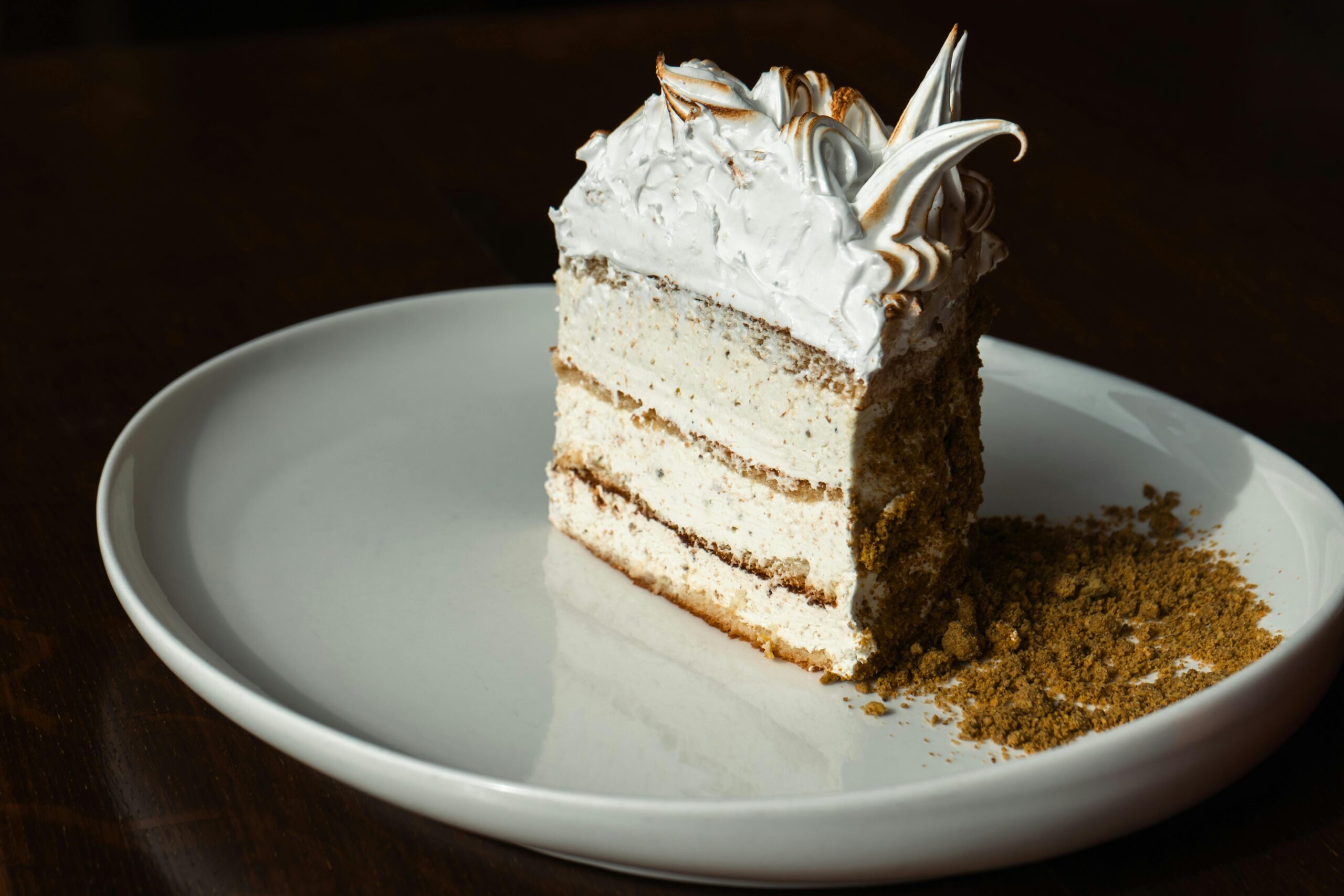 Ein wunderschÃ¶n prÃ¤sentiertes StÃ¼ck Schichtkuchen mit Sahneglasur auf einem weiÃŸen Teller.